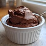 A rich scoop of Vegan Chocolate Avocado Mousse served in a white fluted ramekin with a spoon.