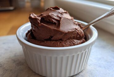 A rich scoop of Vegan Chocolate Avocado Mousse served in a white fluted ramekin with a spoon.