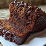 A close-up of a thick slice cut from rich Vegan Chocolate Banana Bread topped with melted chocolate chips.