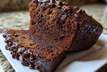 A close-up of a thick slice cut from rich Vegan Chocolate Banana Bread topped with melted chocolate chips.