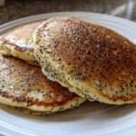 A stack of three fluffy Vegan Lemon Poppy Seed Pancakes with visible poppy seeds on a white plate.