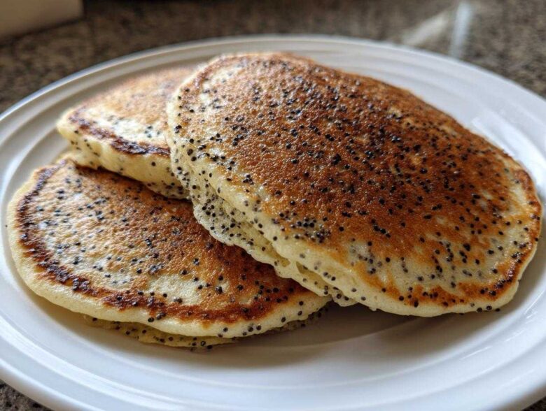 A stack of three fluffy Vegan Lemon Poppy Seed Pancakes with visible poppy seeds on a white plate.