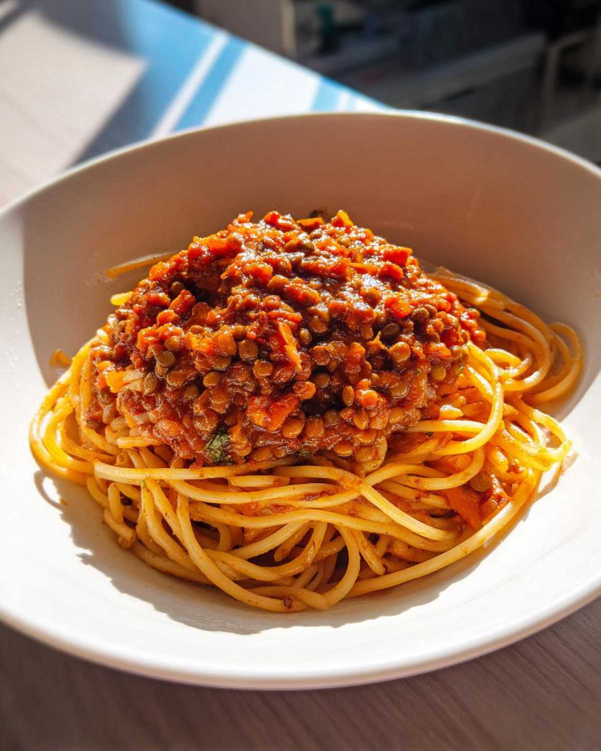 A close-up of spaghetti topped generously with rich Vegan Lentil Bolognese sauce in a white bowl.