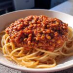 A white bowl filled with spaghetti topped generously with rich Vegan Lentil Bolognese sauce.
