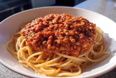 A white bowl filled with spaghetti topped generously with rich Vegan Lentil Bolognese sauce.
