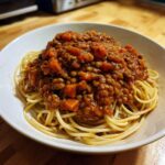A white bowl filled with spaghetti topped generously with rich Vegan Lentil Bolognese sauce.