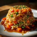 A perfectly molded serving of Vegetable Fried Rice with carrots and peas, drizzled in a rich sauce.