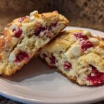 Two halves of a flaky White Chocolate Raspberry Scone showing the interior with bright red raspberries and white chocolate chips.