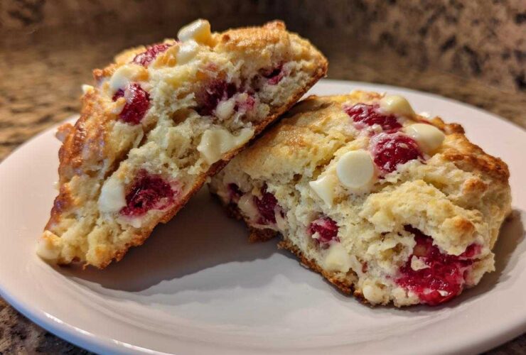 Two halves of a flaky White Chocolate Raspberry Scone showing the interior with bright red raspberries and white chocolate chips.