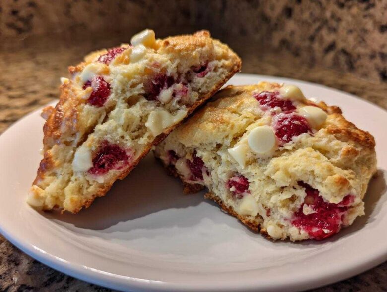 Two halves of a flaky White Chocolate Raspberry Scone showing the interior with bright red raspberries and white chocolate chips.
