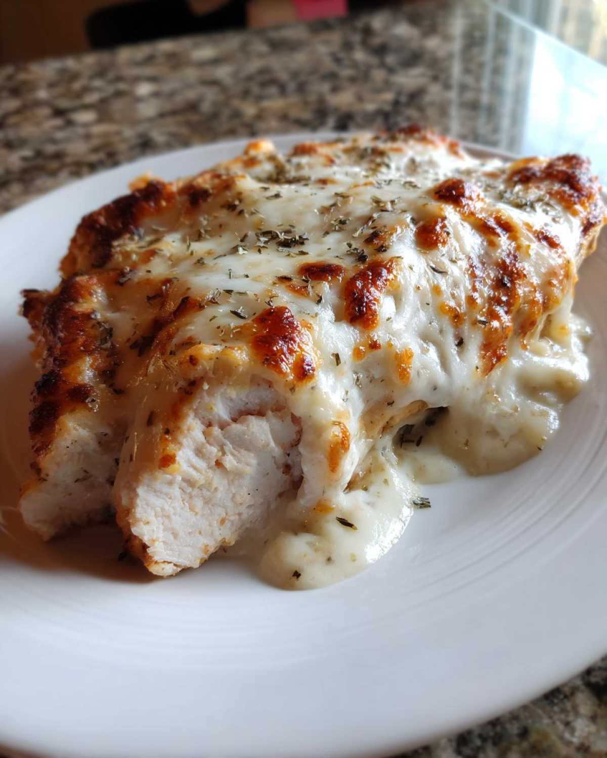 A close-up of a serving of Cheesy Baked Chicken with Cream Sauce, showing melted, browned cheese and herbs over moist white chicken.