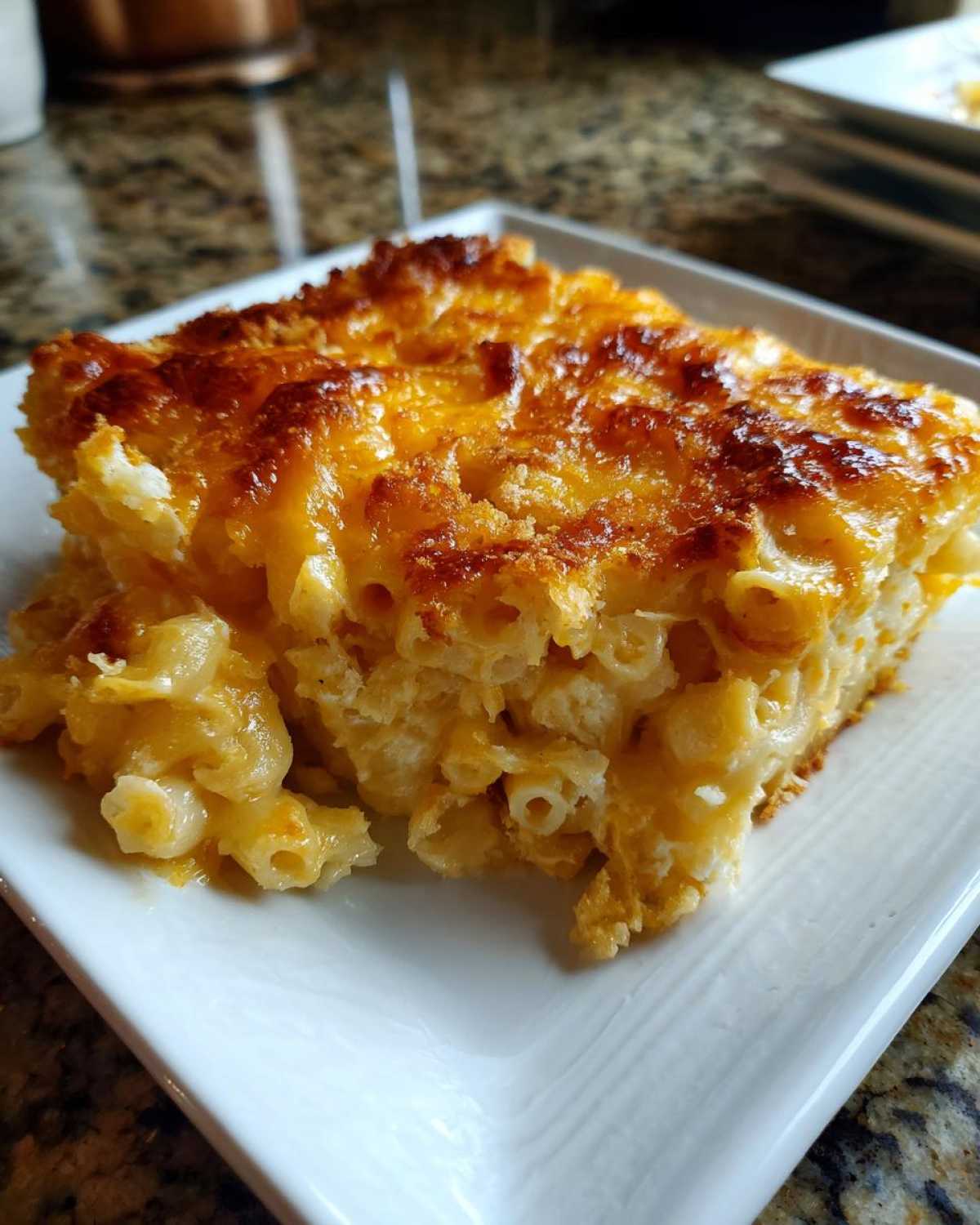 A square serving of Cheesy Baked Mac and Cheese with Crispy Top on a white plate.