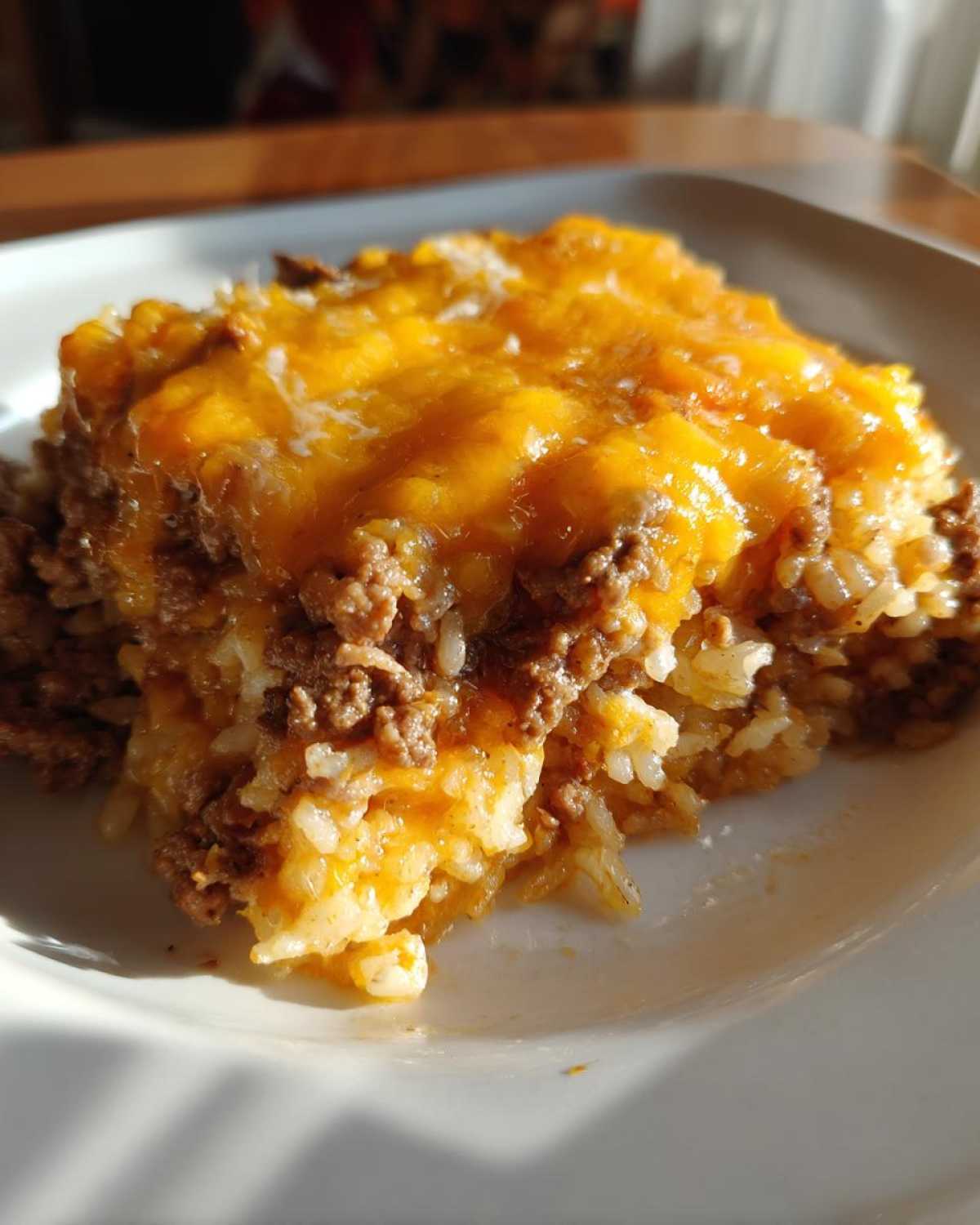 A close-up serving of Cheesy Beef and Rice Casserole Comfort Dish topped with melted orange cheddar cheese.