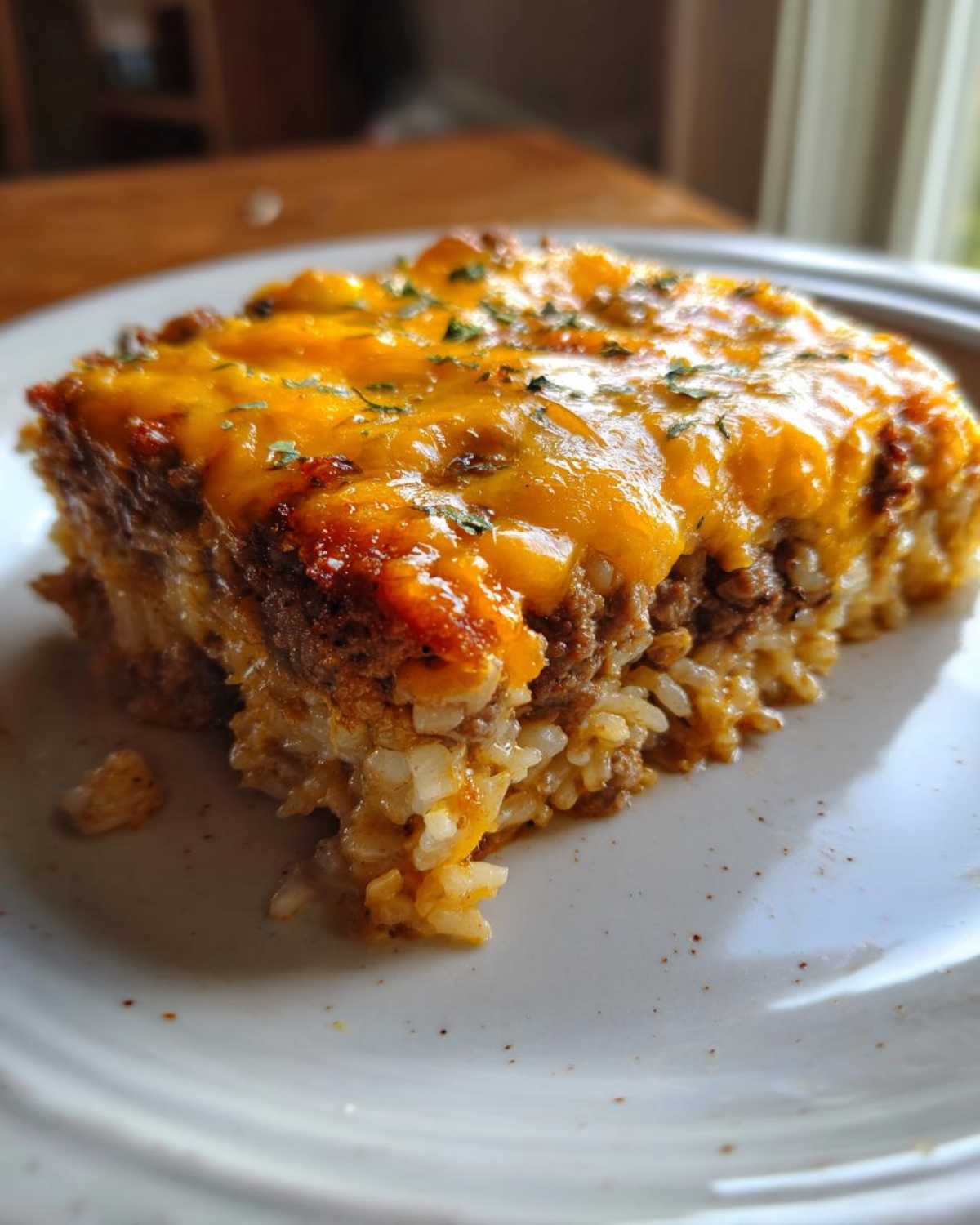 A close-up of a square serving of Cheesy Beef and Rice Casserole Comfort Dish topped with melted cheddar cheese.