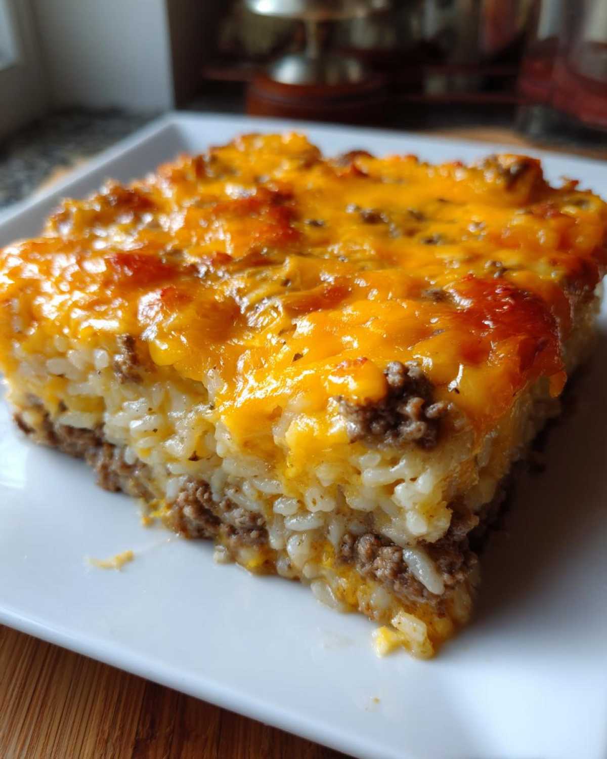 A square slice of Cheesy Beef and Rice Casserole Comfort Dish with melted cheddar cheese on top.