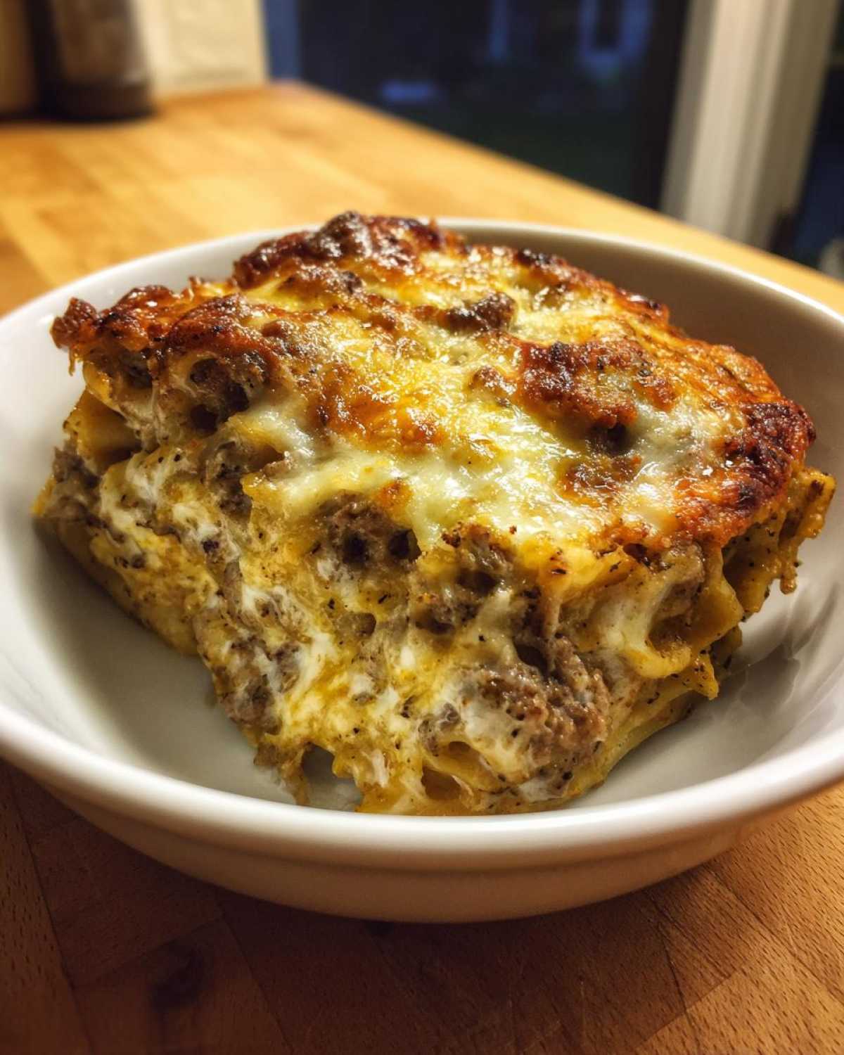 A close-up serving of Cheesy Beef Pasta Bake with Cream Sauce, featuring a golden-brown, bubbly cheese top