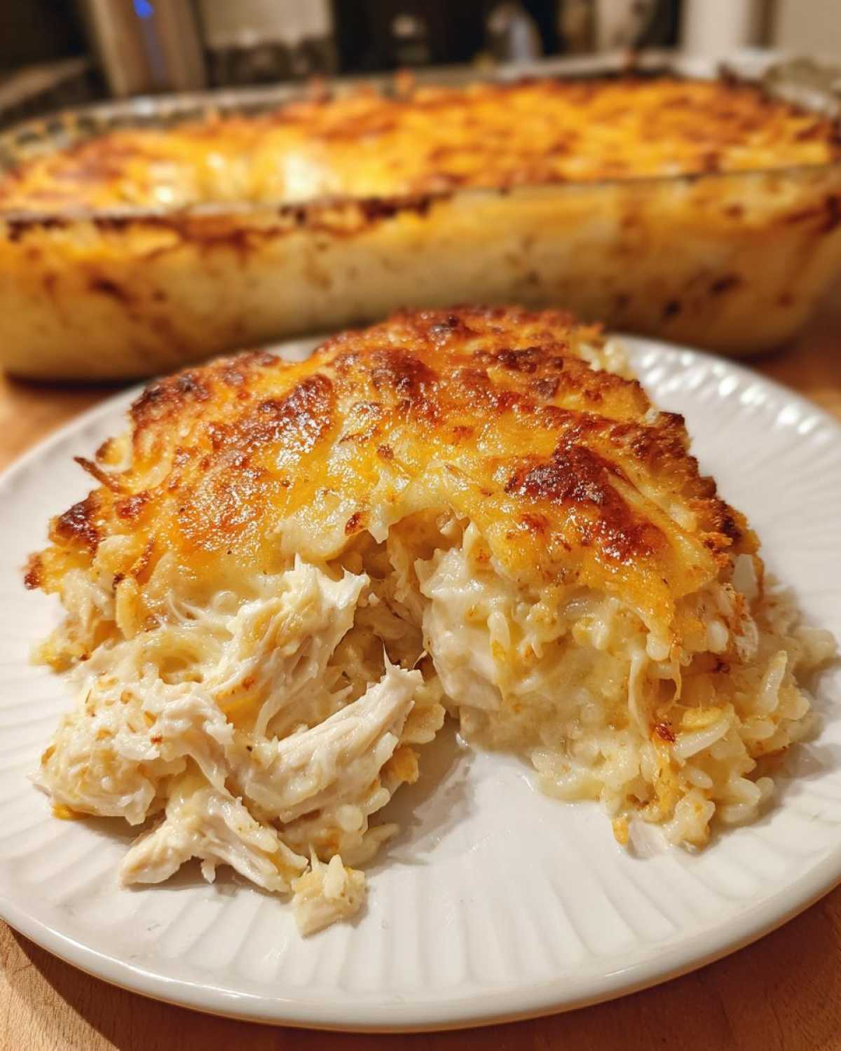 A close-up serving of Cheesy Chicken and Rice Bake with Golden Top, showing shredded chicken and creamy rice under a browned cheese crust.