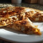 Close-up of a golden-brown Cheesy Chicken Quesadilla with creamy filling, cut into triangles on a white plate.