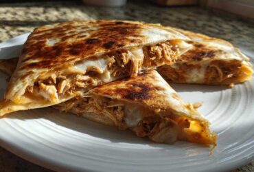 Close-up of a golden-brown Cheesy Chicken Quesadilla with creamy filling, cut into triangles on a white plate.