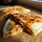 Close-up of crispy, golden-brown Cheesy Chicken Quesadilla triangles revealing shredded chicken and melted cheese filling.