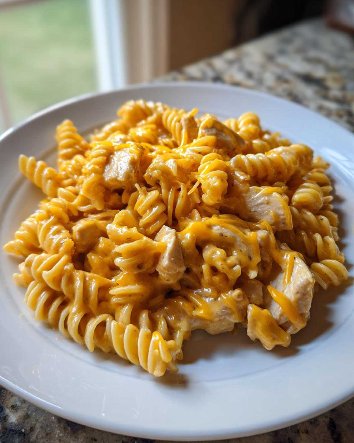 A close-up of Cheesy Chicken Queso Pasta made with rotini pasta and chunks of chicken, served on a white plate.