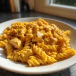 A close-up of Cheesy Chicken Queso Pasta made with fusilli pasta and chunks of seasoned chicken in a rich orange sauce.