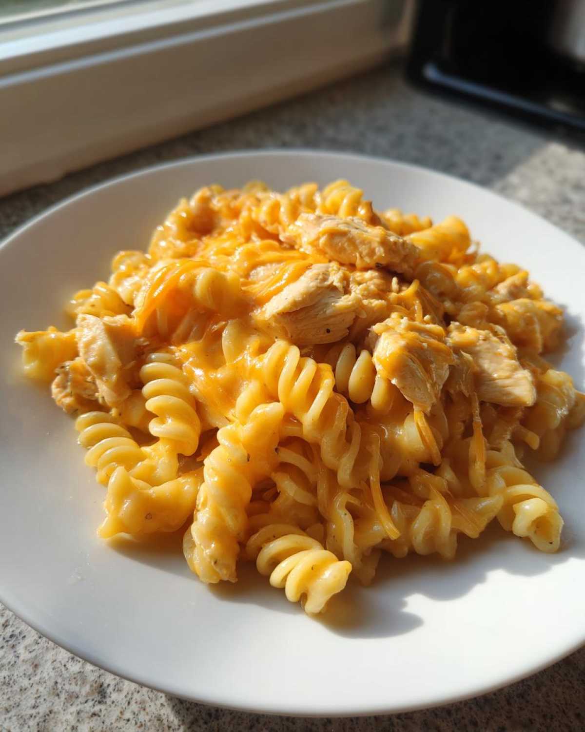 A close-up of rotini pasta mixed with shredded chicken in a bright orange, creamy sauce, representing Cheesy Chicken Queso Pasta Creamy and Rich.