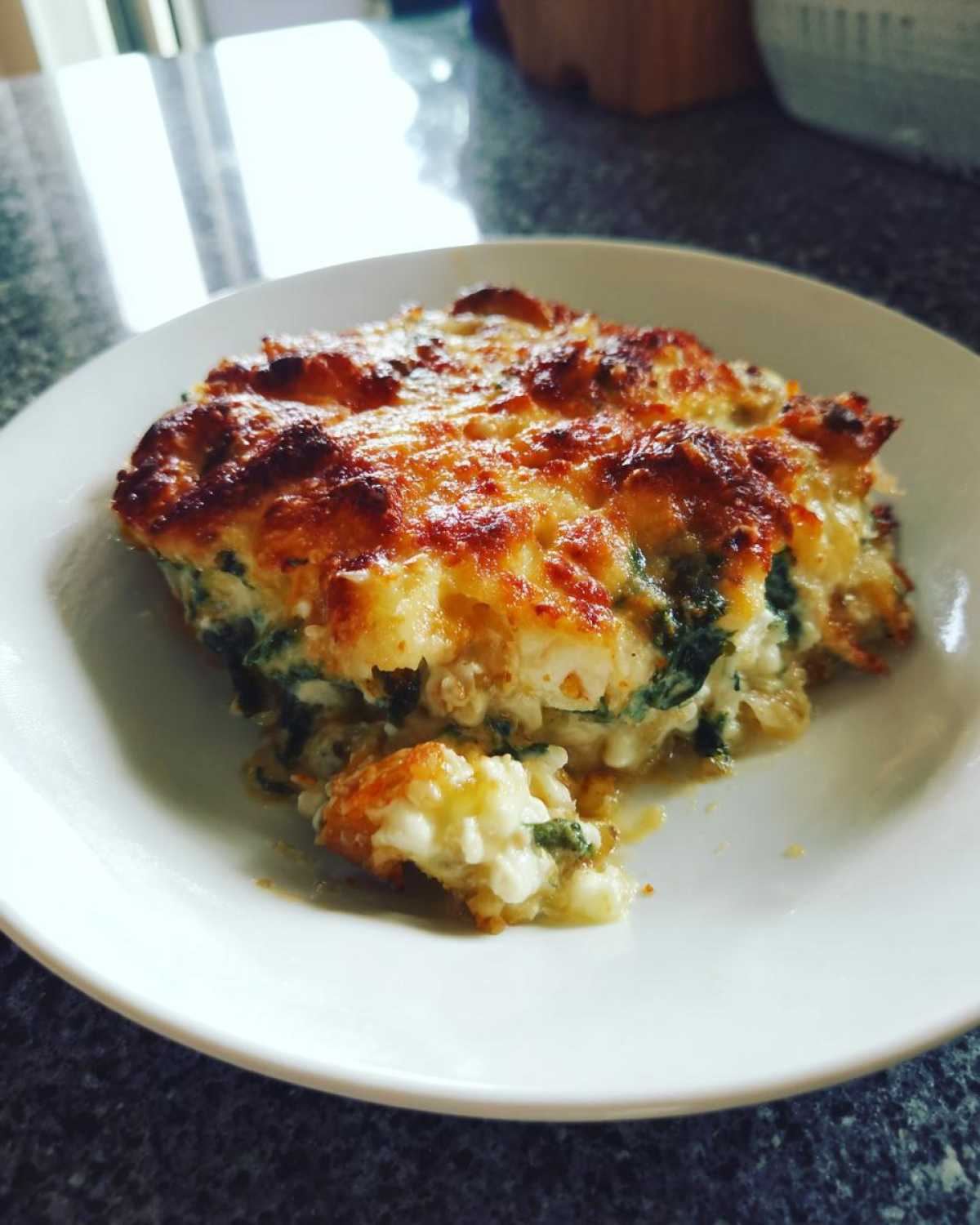 A serving of Cheesy Chicken and Spinach Bake Comfort Meal with a golden, bubbly cheese topping on a white plate.