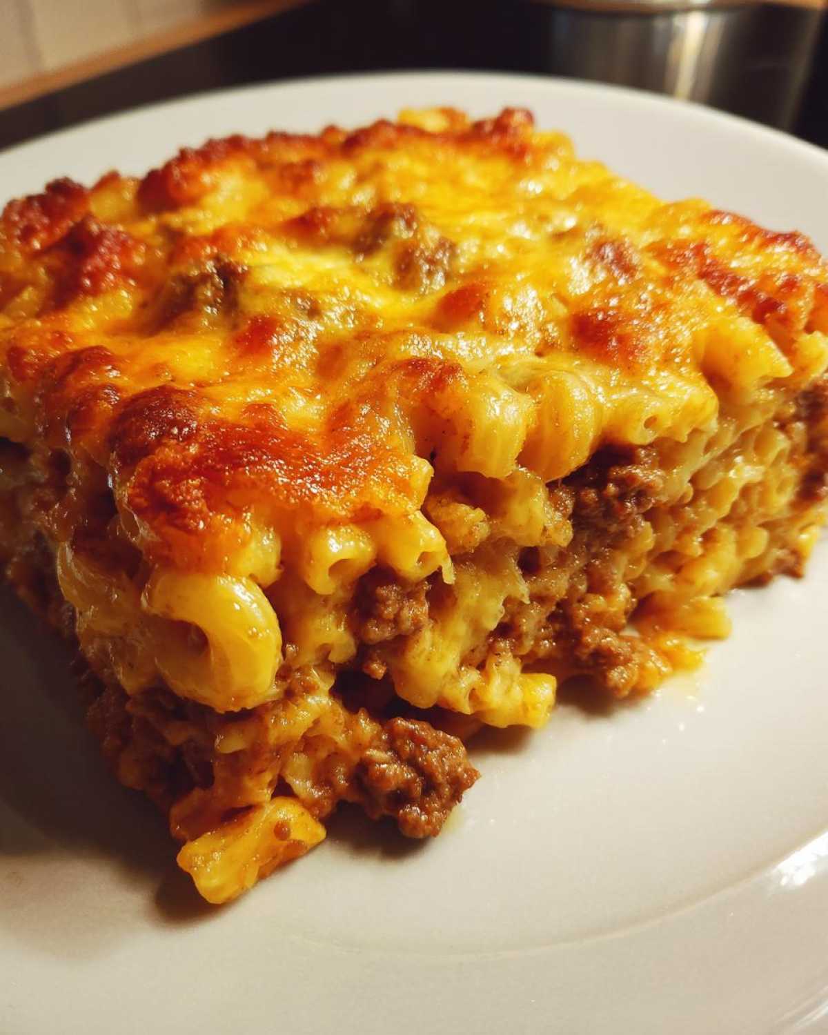 A close-up of a square slice of Cheesy Ground Beef Pasta Bake Comfort Food with a bubbly, browned cheese topping.