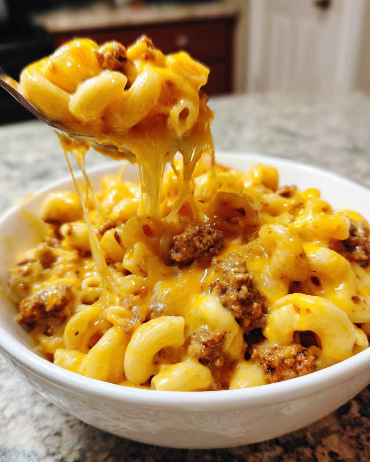 A spoonful of Cheesy Ground Beef Pasta with Creamy Sauce showing a dramatic cheese pull over a white bowl.