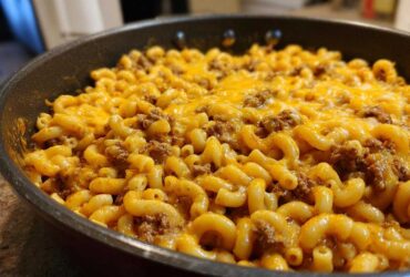 Close-up of Cheesy Ground Beef Pasta Skillet Comfort Food featuring elbow macaroni, ground beef, and melted cheddar cheese in a black skillet.