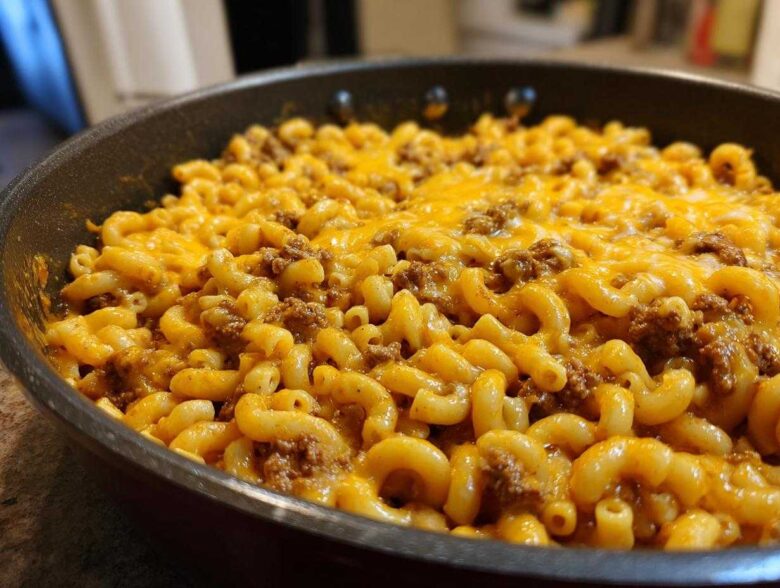 Close-up of Cheesy Ground Beef Pasta Skillet Comfort Food featuring elbow macaroni, ground beef, and melted cheddar cheese in a black skillet.