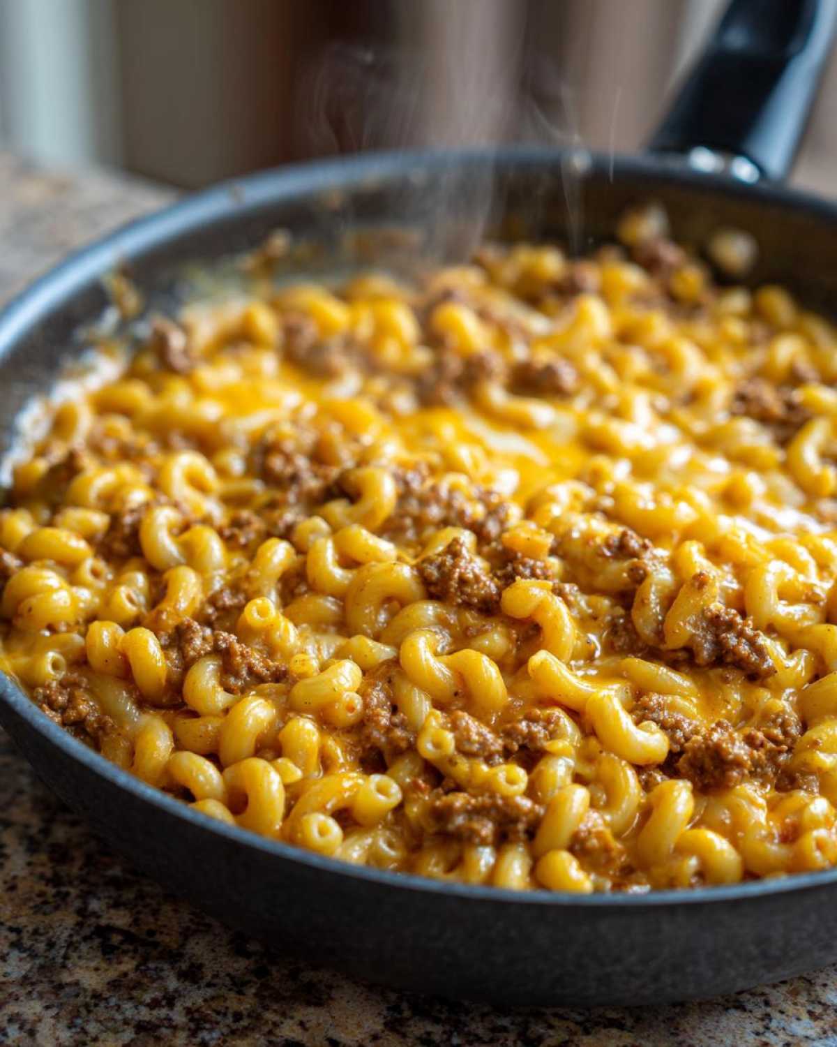 Close-up of steaming Cheesy Ground Beef Pasta Skillet Comfort Food with elbow macaroni and melted cheddar cheese.