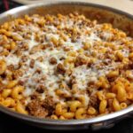 Close-up of Cheesy Ground Beef Pasta Skillet topped with melted mozzarella cheese in a stainless steel pan.