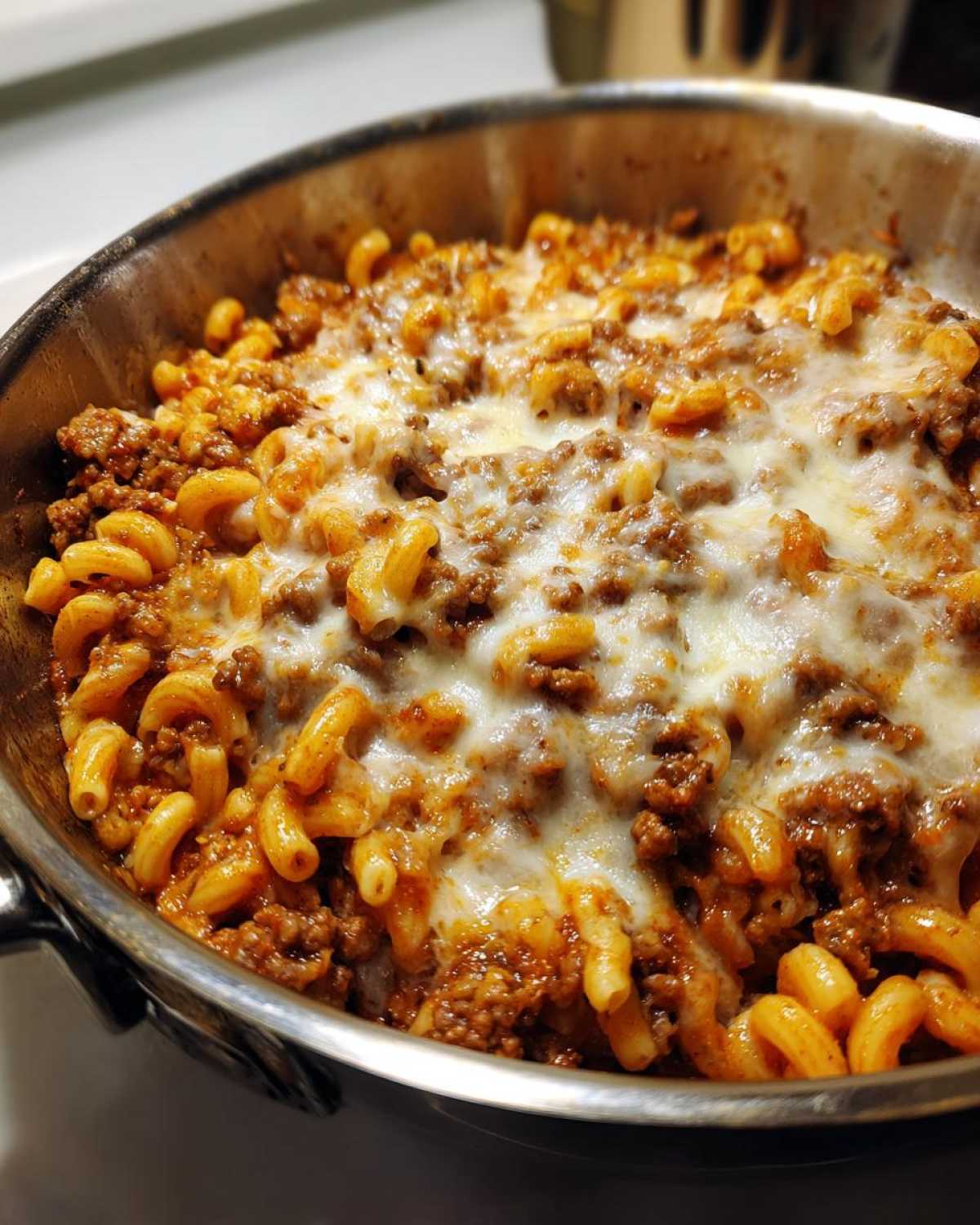 Close-up of Cheesy Ground Beef Pasta Skillet topped with melted mozzarella cheese in a stainless steel pan.