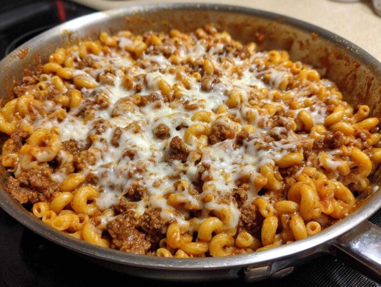 Close-up of Cheesy Ground Beef Pasta Skillet topped with melted mozzarella cheese in a stainless steel pan.