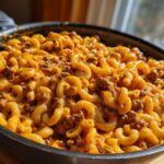 Close-up of Cheesy Taco Pasta One Pot Dinner Idea cooked in a black skillet, featuring elbow macaroni, ground meat, and melted orange cheese.