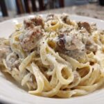 A close-up of a serving of Creamy Alfredo Chicken Pasta with fettuccine noodles and seasoned chicken pieces.