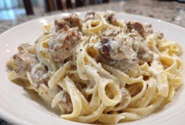 A close-up of a serving of Creamy Alfredo Chicken Pasta with fettuccine noodles and seasoned chicken pieces.