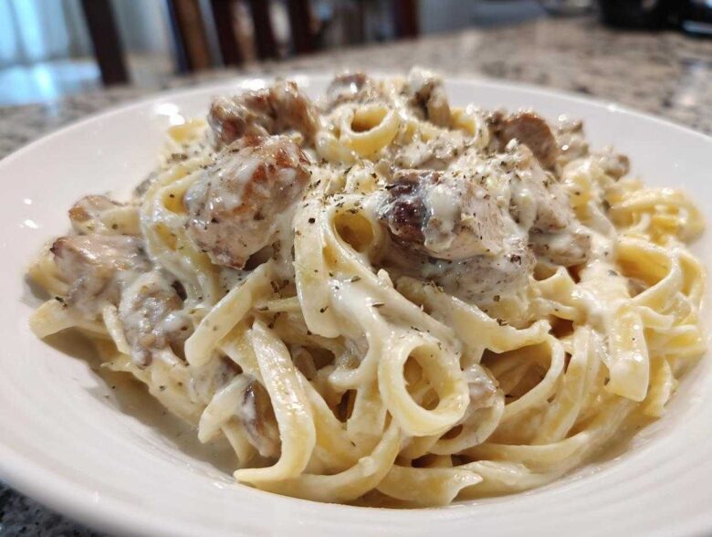 A close-up of a serving of Creamy Alfredo Chicken Pasta with fettuccine noodles and seasoned chicken pieces.