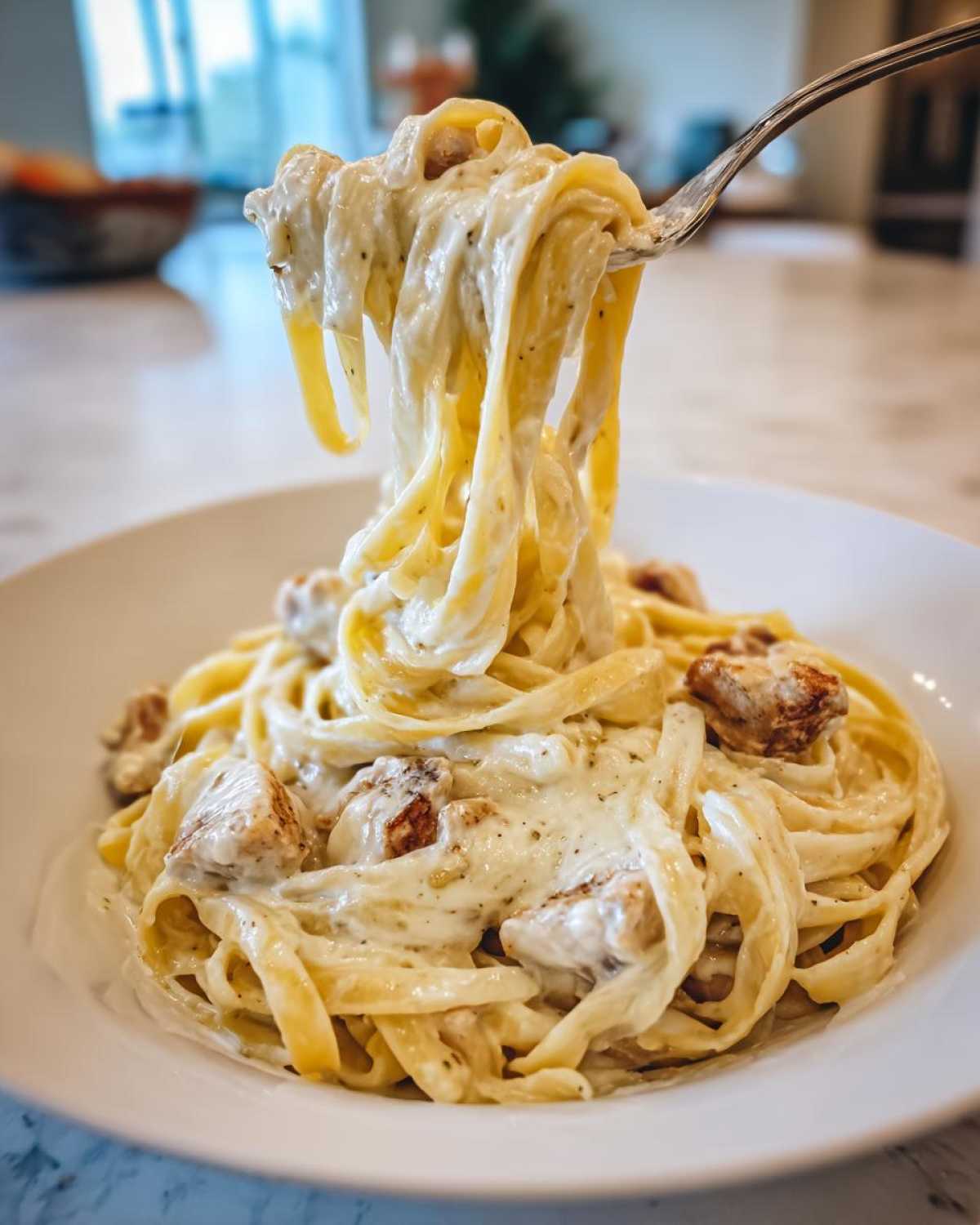 A fork lifting fettuccine noodles coated in rich white sauce from a bowl of Creamy Alfredo Chicken Pasta Easy Recipe.