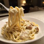 A fork lifts fettuccine noodles coated in rich sauce from a bowl of Creamy Alfredo Chicken Pasta Easy Recipe.