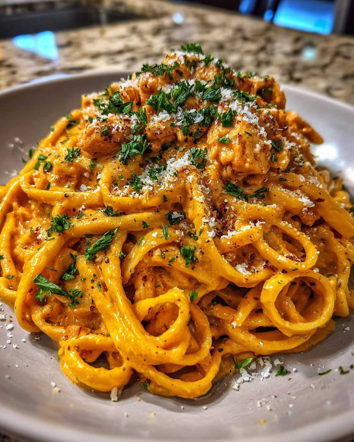 Close-up of a bowl of Creamy Cajun Chicken Alfredo pasta coated in rich orange sauce, topped with parsley and cheese.