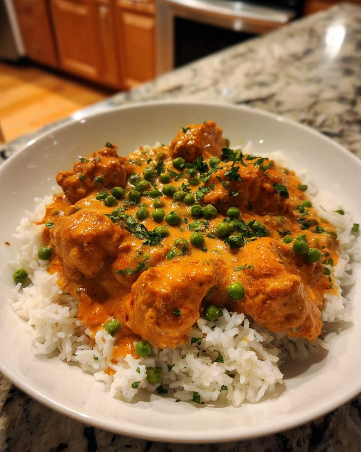 A bowl of white rice topped with creamy, orange-hued Creamy Cajun Chicken Skillet with Rice and green peas.