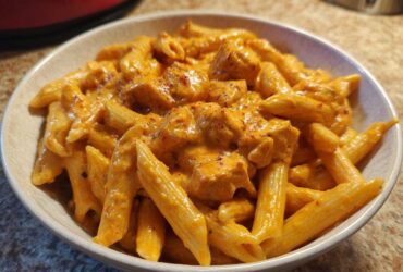 A close-up of a bowl filled with Creamy Cajun Pasta with Chicken and Spice, coated in a rich orange sauce.