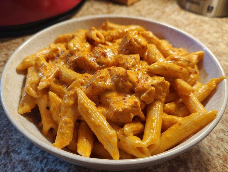 A close-up of a bowl filled with Creamy Cajun Pasta with Chicken and Spice, coated in a rich orange sauce.