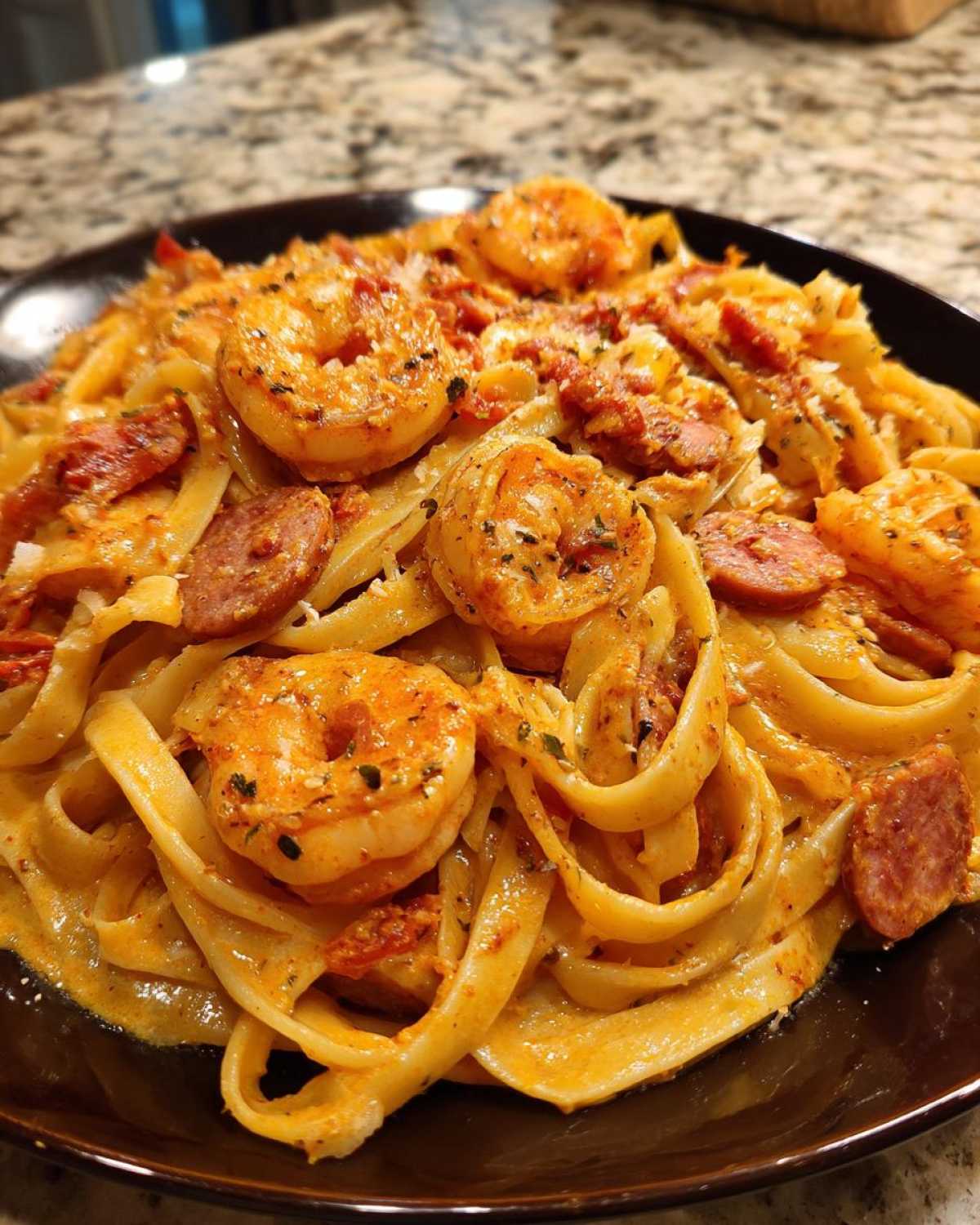 A close-up view of Creamy Cajun Shrimp Pasta featuring fettuccine noodles, seasoned shrimp, and slices of andouille sausage in a rich sauce.