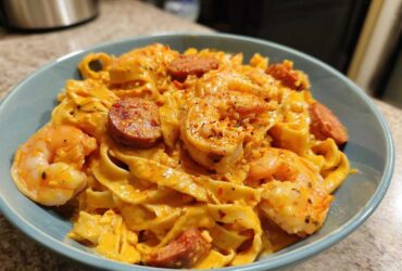 A close-up of a bowl filled with Creamy Cajun Shrimp Pasta featuring fettuccine, plump shrimp, and sliced smoked sausage.