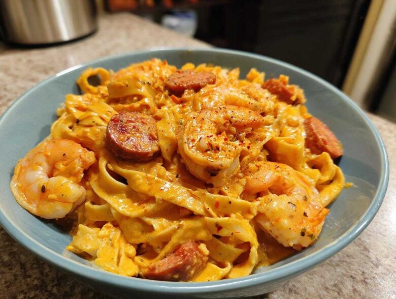 A close-up of a bowl filled with Creamy Cajun Shrimp Pasta featuring fettuccine, plump shrimp, and sliced smoked sausage.