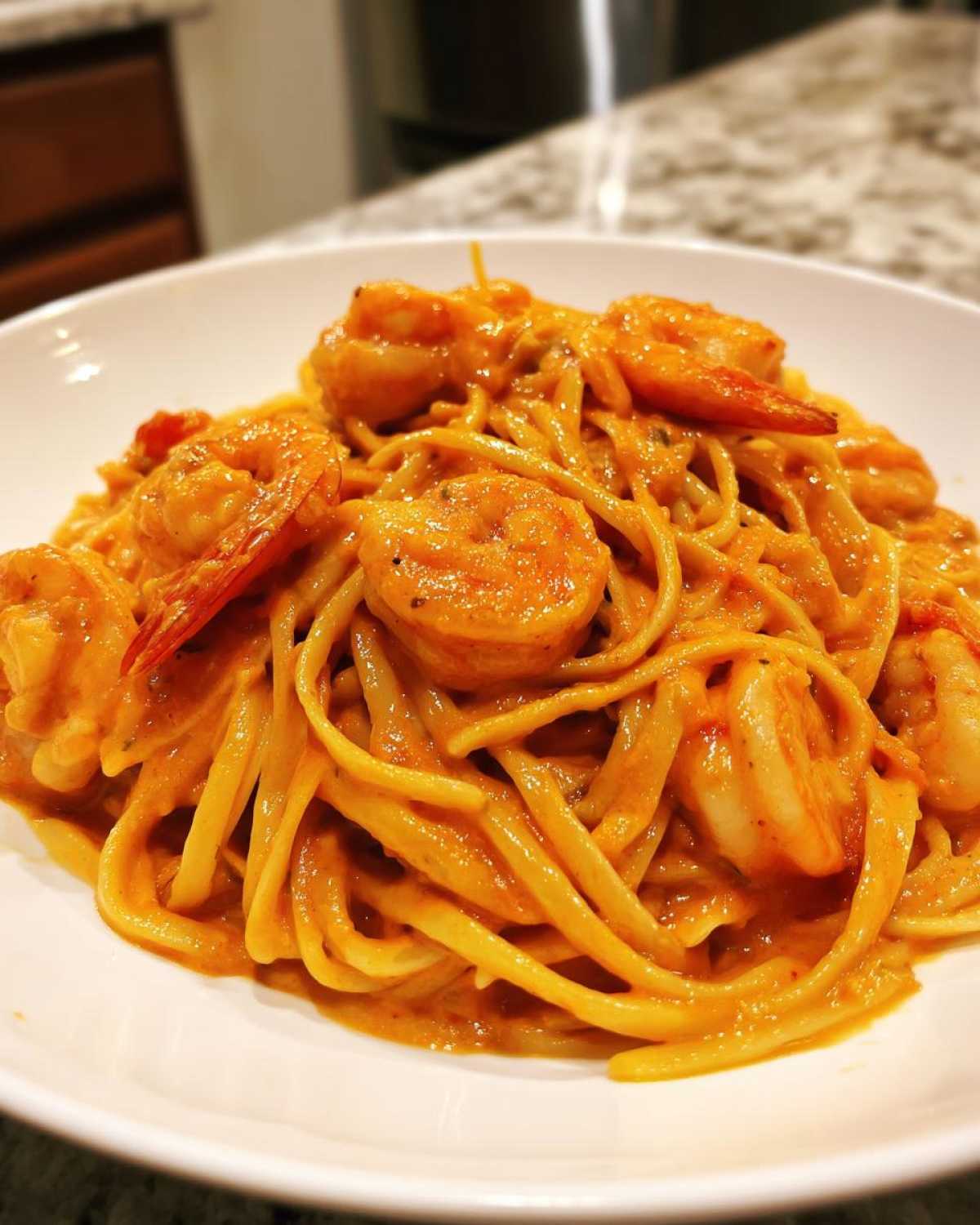 A close-up of a white bowl filled with Creamy Cajun Shrimp Pasta, featuring linguine coated in a rich, orange-hued sauce and topped with large shrimp.